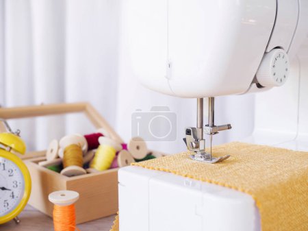 Téléchargez les photos : Gros plan machine à coudre travaillant avec du tissu jaune, accessoires de couture sur la table, couture de nouveaux vêtements. - en image libre de droit