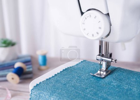 Téléchargez les photos : Cloe up machine à coudre travaillant avec du tissu bleu, accessoires de couture sur la table, coudre de nouveaux vêtements. - en image libre de droit