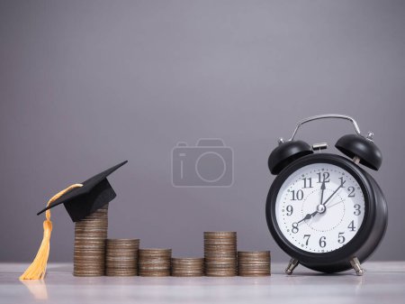 Black alarm clock, Graduation hat and stack of coins. The concept of saving money, manage time to success for education, student loan, scholarship, tuition fees in the future