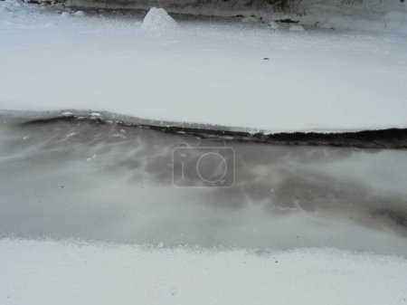 Close up : Frozen Ostravice river in Czech mountains covered by a layer of cracked partially transparent ice and snow during snowy winter day