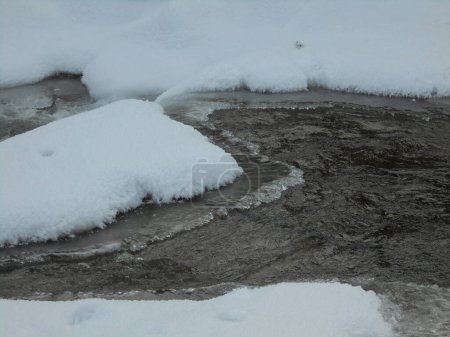 Gefrierender wilder Fluss, der durch die verschneite Natur der tschechischen Berge fließt, wobei Eis auf der Oberfläche bleibt