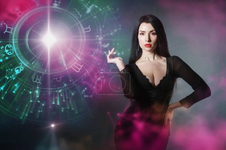 Photo for Astrology. Horoscope. A portrait of a brunette girl with a piercing look stands on a dark background with the signs of the zodiac - Royalty Free Image