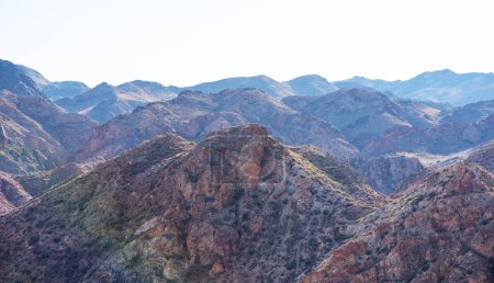 view of a mountain range with textures of the rocks and varied shades. The mountains a rugged appearance, with sharp peaks and deep crevices. The color palette is a mix of warm earth tones