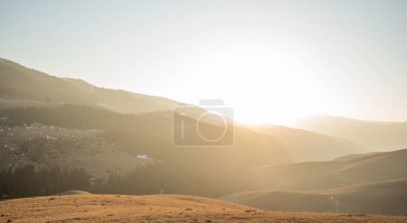 La suave luz del sol se filtra sobre ondulantes colinas cubiertas de hierba, proyectando un cálido resplandor en el sereno paisaje de las tierras altas con siluetas de montaña distantes..
