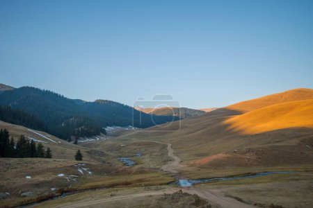 the serene beauty of a mountainous landscape at dusk, with the last rays of sunlight casting a warm glow on the rolling hills and a meandering stream