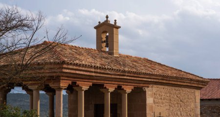 classic Mediterranean building with a terracotta tiled roof and a bell tower, set against a cloudy sky, with tree branches in the foreground