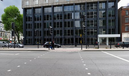 Foto de Londres - 05 07 2022: Hombre esperando en el cruce peatonal de Euston Rd revisando su teléfono móvil. - Imagen libre de derechos