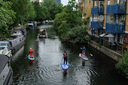 Photo for London - 05 21 2022: Paddleboarders along Grand Union Canal with ship and houseboats - Royalty Free Image