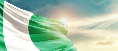 Photo for Nigeria waving flag in beautiful sky with sun - Royalty Free Image