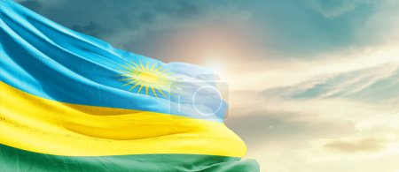 Téléchargez les photos : Drapeau du Rwanda agitant dans un ciel magnifique avec soleil - en image libre de droit