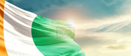 Téléchargez les photos : Drapeau de l'île d'Ivoire agitant dans un ciel magnifique avec soleil - en image libre de droit