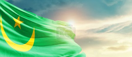 Téléchargez les photos : Mauritania waving flag in beautiful sky with sun - en image libre de droit