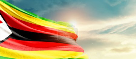 Téléchargez les photos : Zimbabwe agitant le drapeau dans un ciel magnifique avec le soleil - en image libre de droit