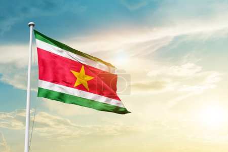 Téléchargez les photos : Suriname waving flag in beautiful sky with sun - en image libre de droit