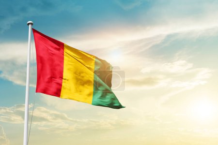 Foto de Bandera de Guinea ondeando en hermoso cielo con sol - Imagen libre de derechos
