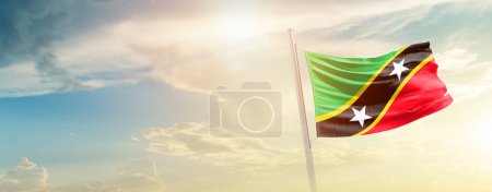 Foto de Saint Kitts and Nevis waving flag in beautiful sky with sun - Imagen libre de derechos