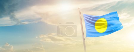 Téléchargez les photos : Palau waving flag in beautiful sky with sun - en image libre de droit