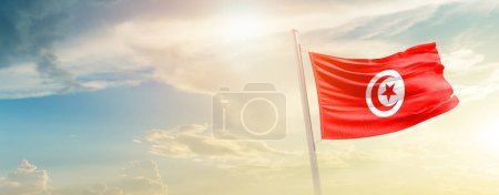 Téléchargez les photos : Tunisie agitant drapeau dans un ciel magnifique avec soleil - en image libre de droit