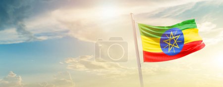 Photo for Ethiopia waving flag in beautiful sky with sun - Royalty Free Image