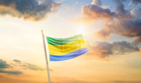 Téléchargez les photos : Drapeau du Gabon agitant dans un ciel magnifique avec nuages et soleil - en image libre de droit