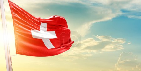 Téléchargez les photos : Drapeau de la Suisse contre le ciel avec nuages et soleil - en image libre de droit
