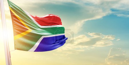 Foto de Bandera de Sudáfrica contra el cielo con nubes y sol - Imagen libre de derechos