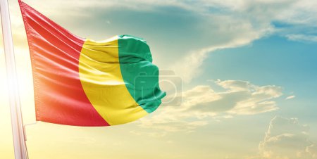 Téléchargez les photos : Drapeau de Guinée contre ciel avec nuages et soleil - en image libre de droit