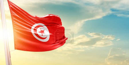Téléchargez les photos : Drapeau Tunisie contre ciel avec nuages et soleil - en image libre de droit