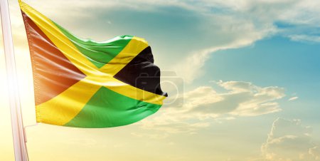 Téléchargez les photos : Drapeau de la Jamaïque contre le ciel avec nuages et soleil - en image libre de droit