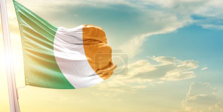 Foto de Bandera de Irlanda contra el cielo con nubes y sol - Imagen libre de derechos