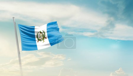 Téléchargez les photos : Guatemala agitant le drapeau contre le ciel bleu avec des nuages - en image libre de droit