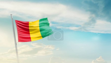 Guinea waving flag against blue sky with clouds