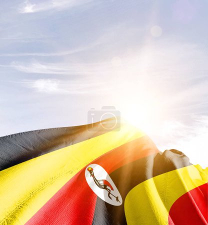 Uganda waving flag against blue sky with clouds