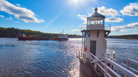 Photo for Image of Large commercial ship on Maine river sails past small lighthouse with blue skies - Royalty Free Image