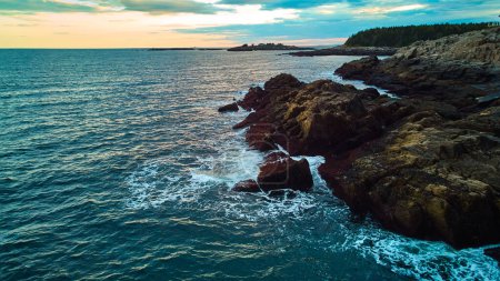 Téléchargez les photos : Image de Serene vue sur l'océan au-dessus des côtes du Maine avec des côtes rocheuses, vagues s'écrasant, et la lumière du coucher du soleil - en image libre de droit