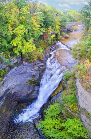 Téléchargez les photos : Image de cascade dans le canyon entouré d'arbres d'automne avec pont en arc de pierre en arrière-plan - en image libre de droit
