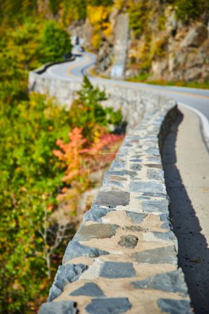 Foto de Imagen de Hermosa pared de piedra serpenteando a lo largo de la carretera que zig zags a través de acantilados de montaña en la distancia - Imagen libre de derechos