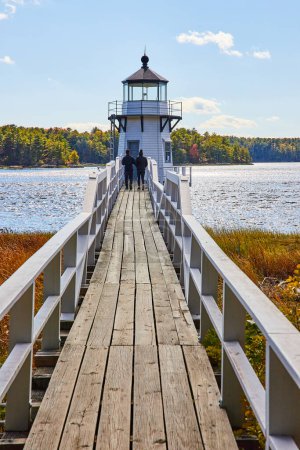Photo for Image of Wood bridge leads to small white Maine lighthouse with two tourists walking - Royalty Free Image