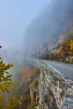 Foto de Imagen de la mañana brumosa en la carretera a través de acantilados junto a la pared de piedra - Imagen libre de derechos