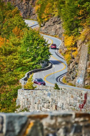 Foto de Imagen de un camino sinuoso con coches y muros de piedra que suben por acantilados y bosques - Imagen libre de derechos