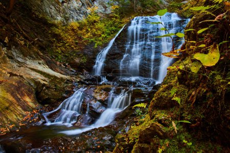 Téléchargez les photos : Image de Grande chute d'eau enragée dans une gorge serrée entourée de roches moussues et de feuilles d'automne - en image libre de droit