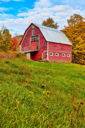Image de Grande grange de campagne vintage rouge dans les champs herbeux avec des arbres d'automne derrière