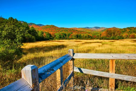 Téléchargez les photos : Image de clôture en bois à côté de grands champs jaunes avec des montagnes d'automne colorées au loin - en image libre de droit