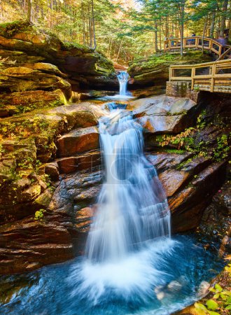 Téléchargez les photos : Image de Superbe vue large sur les cascades du New Hampshire nichées dans une forêt d'automne luxuriante et une promenade donnant sur les touristes - en image libre de droit