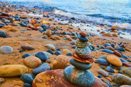 Photo for Image of Cairn of stacked smooth lakebed stones with sandy shore and crashing blue waves - Royalty Free Image