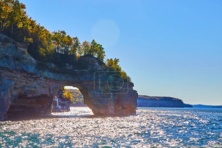 Photo for Image of Sunny waters on great lake with archway in pictured rocks and green forest atop the cliff walls - Royalty Free Image