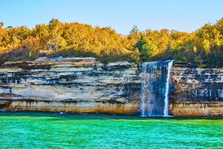 Image of Waterfall cascading off Pictured Rocks cliff wall with multiple mineral colors painting the rocks