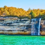 Image of Waterfall cascading off Pictured Rocks cliff wall with multiple mineral colors painting the rocks