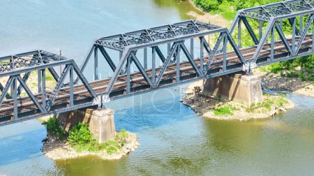 Photo for Image of Aerial blue metal bridge with dual train tracks over river water leading to green bank aerial - Royalty Free Image