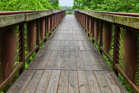 Photo for Image of Long view of bridge with worn planks and rusty rising sun pattern on railing bars - Royalty Free Image